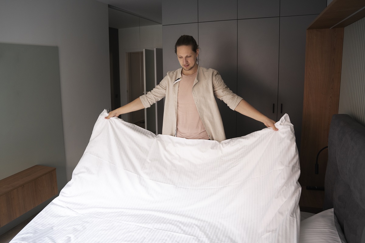 Homem arrumando sua roupa de cama em hótel Homem arrumando sua roupa de cama em hótel